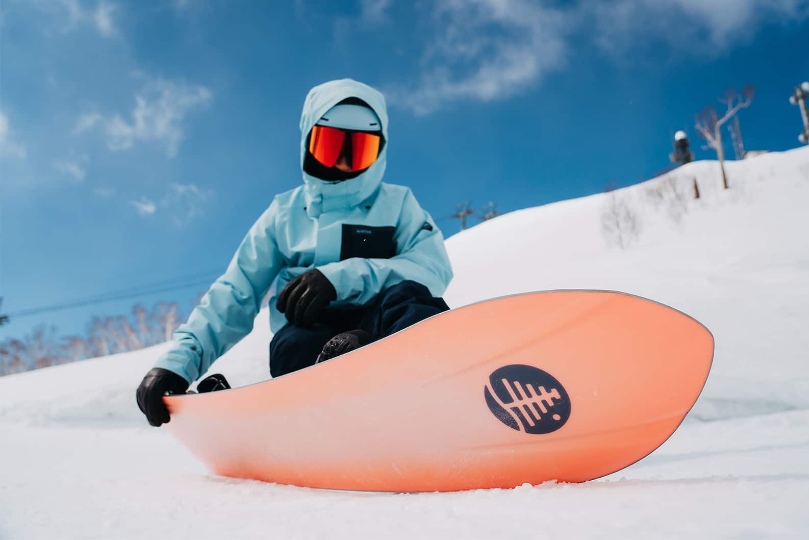 3d Snowboard: Rider sitting on a slope, strapped into a 3D snowboard from Burton’s Family Tree line.