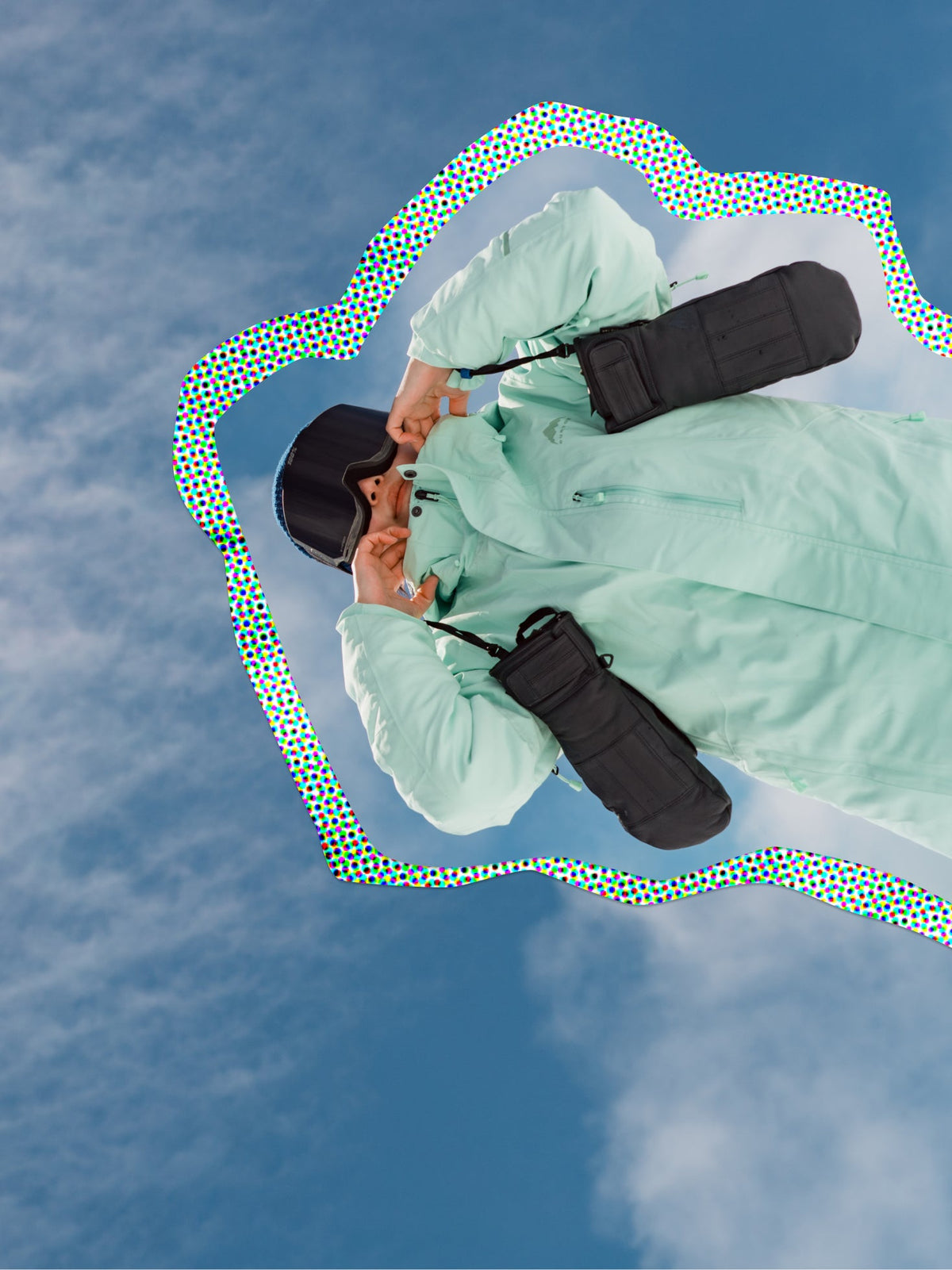 snowboarder holding gloves in front of a cloudy, blue sky