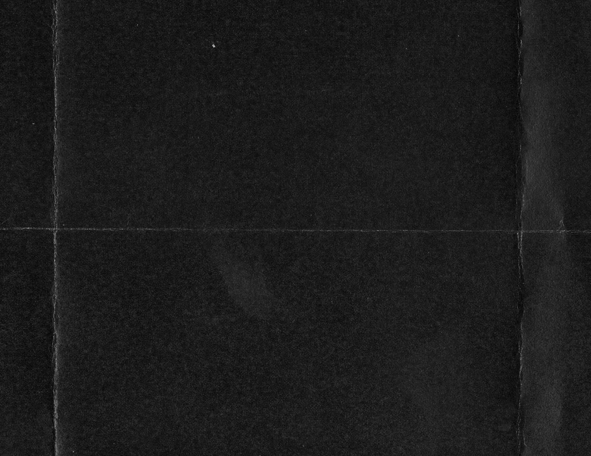 A close-up of a dark textured surface, likely black fabric or material swatch, with a subtle horizontal seam and vertical panel lines.