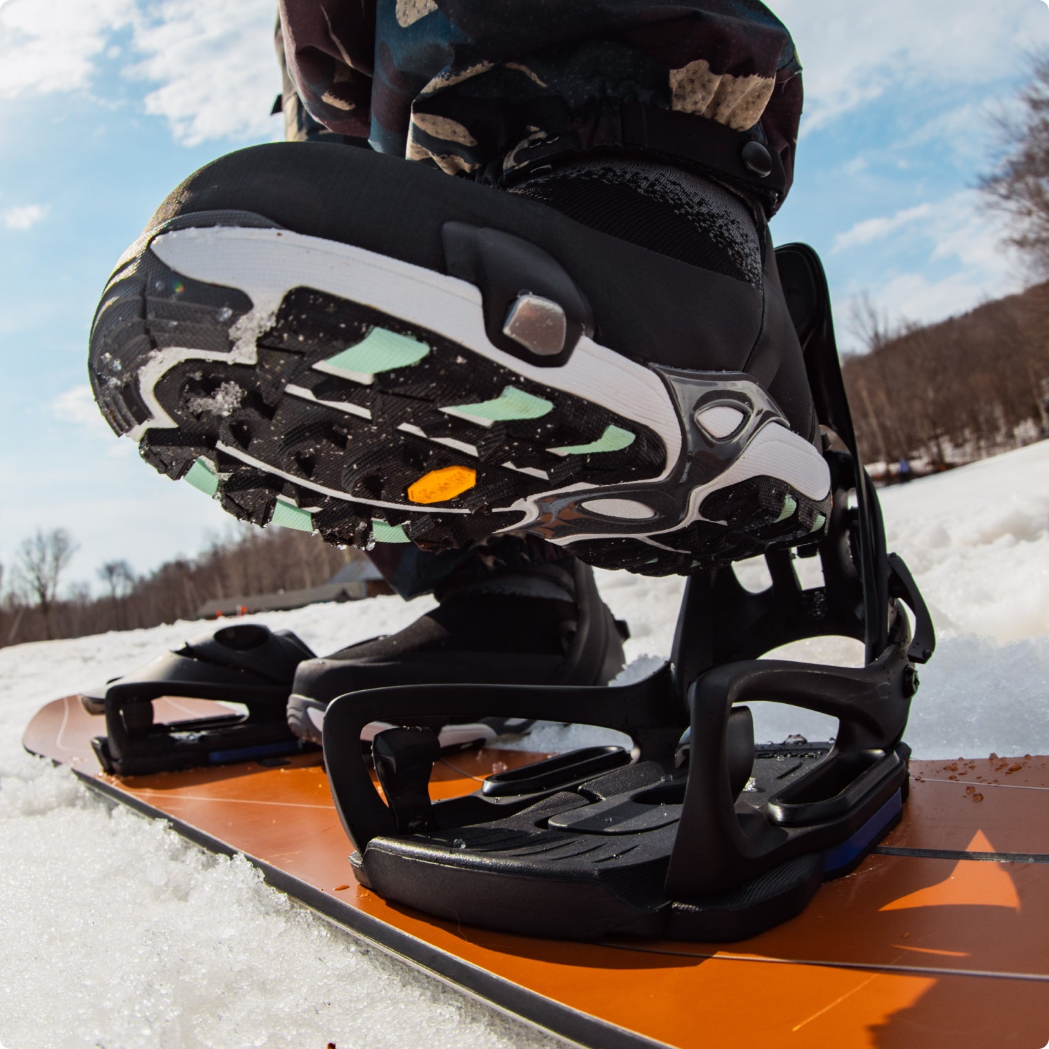 Close-up of a snowboarder's Step On boot and bindings on an orange snowboard in the snow.