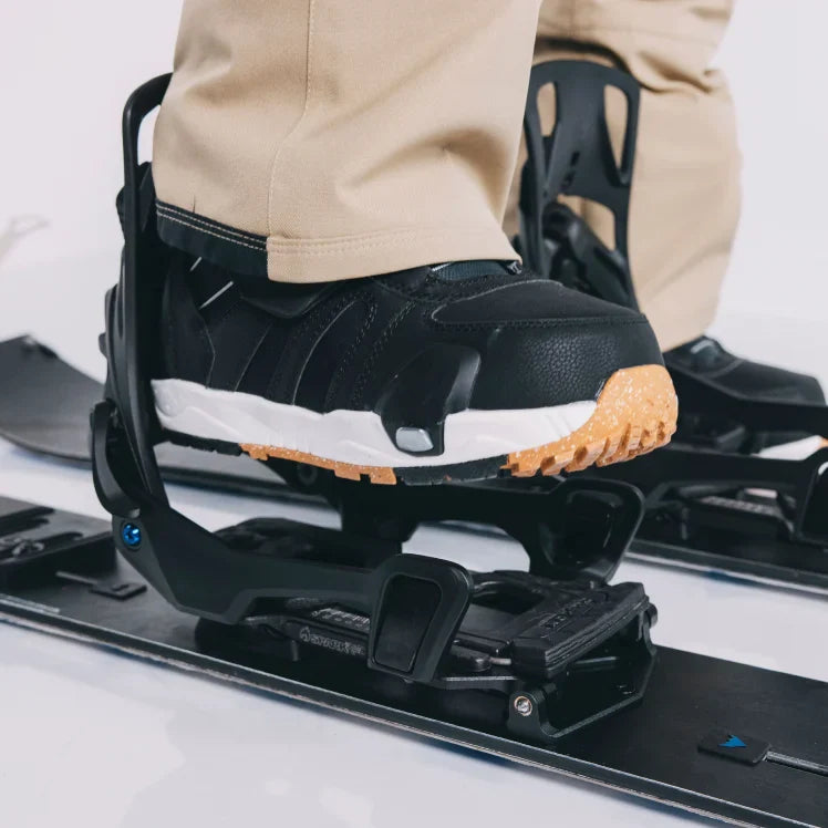 Person wearing a black snowboard boot with a white sole on a snowboard