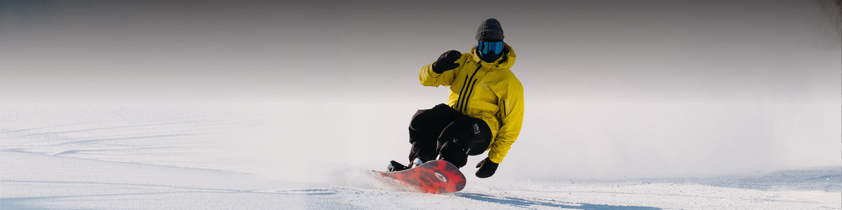 Person snowboarding on a snowy slope with a yellow jacket and goggles.