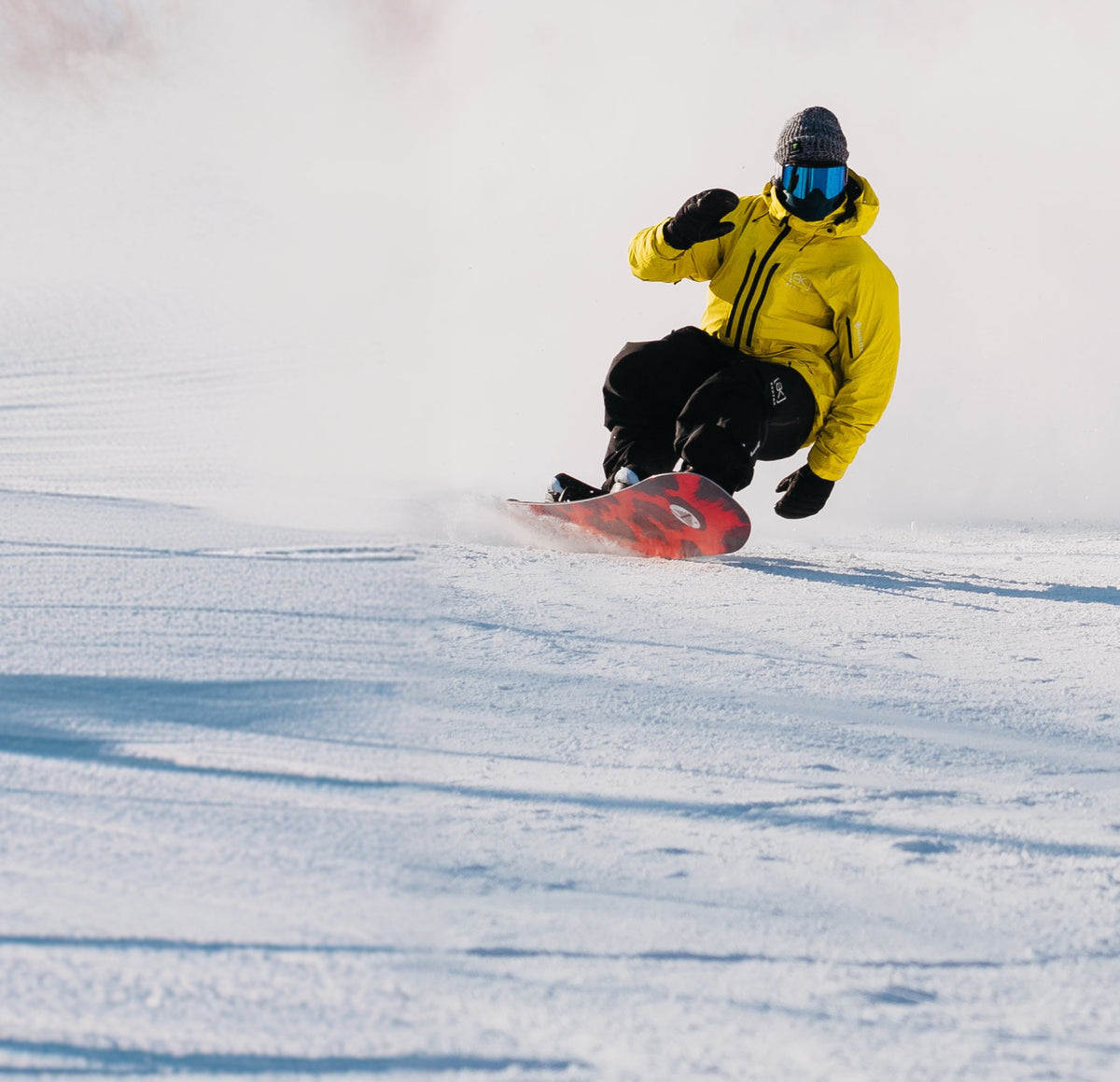 Person snowboarding down a snowy slope wearing a yellow jacket and black pants.