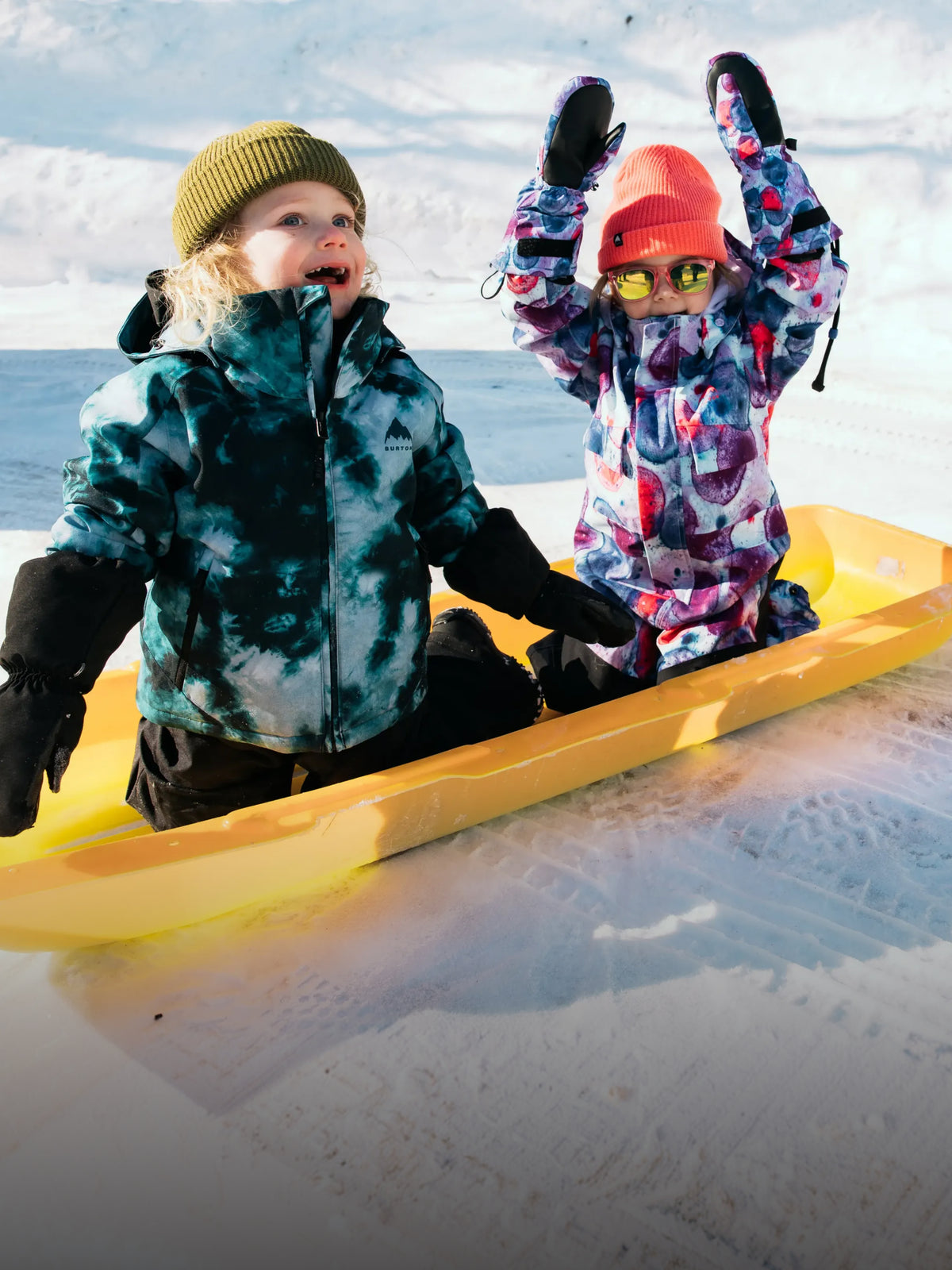Two kids playing in the snow wearing Burton outerwear.
