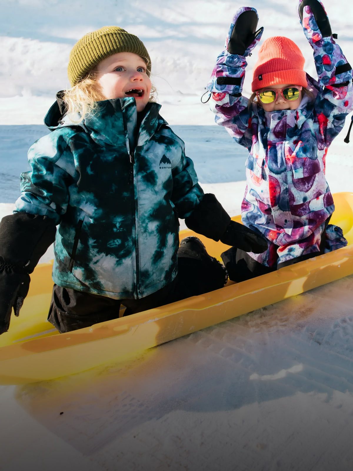 Two kids playing in the snow wearing Burton outerwear.