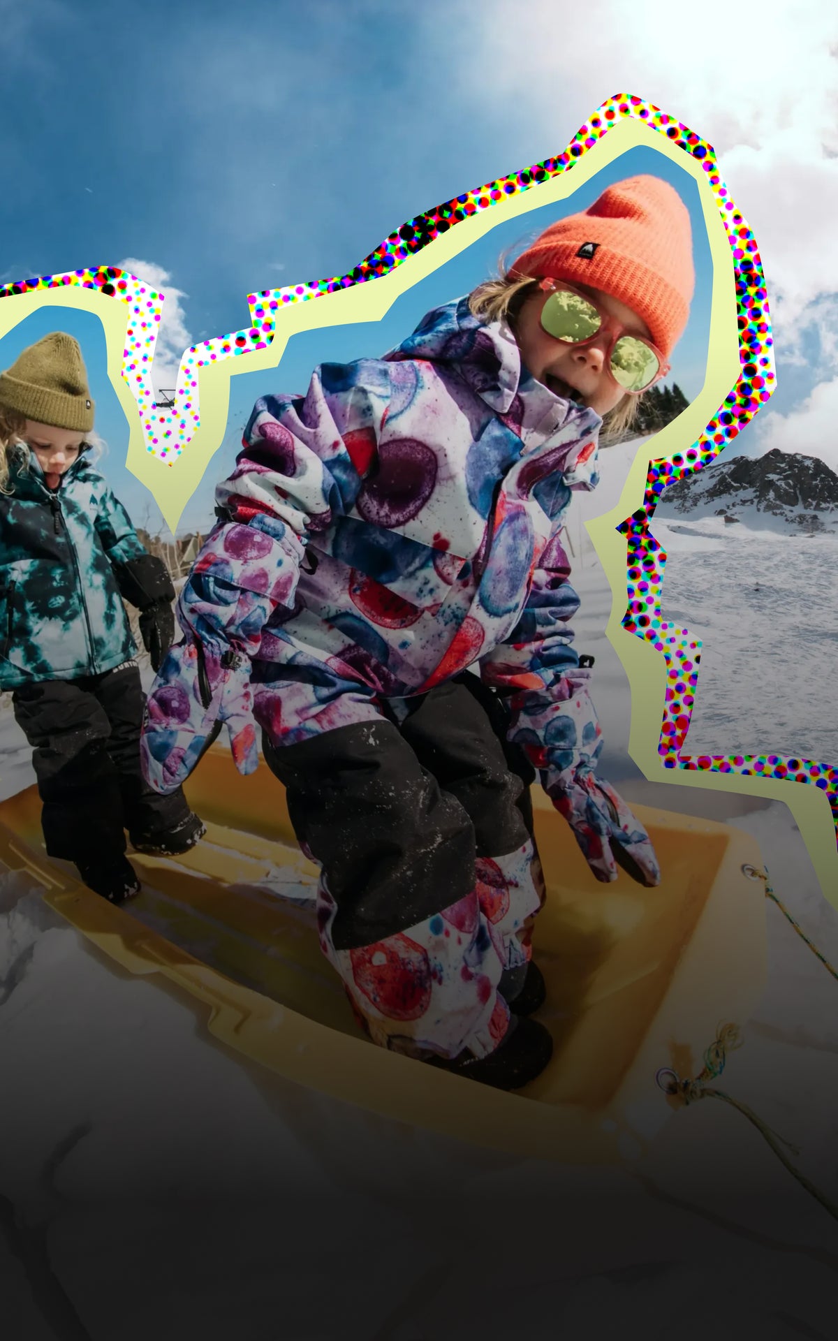 Two kids wearing Burton outerwear and beanies standing on a yellow sled in the snow.