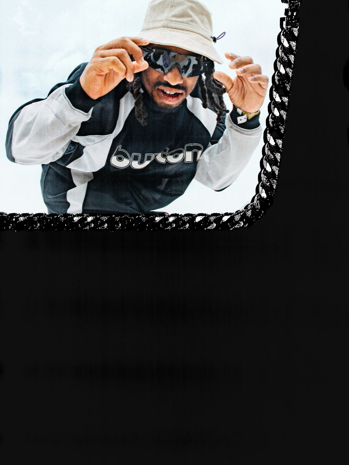Snowboarder Zeb Powell wearing a black and white Burton long sleeved shirt, white pants, and a beige bucket hat, with a large black chain graphic framing the image and black blocks at the bottom.