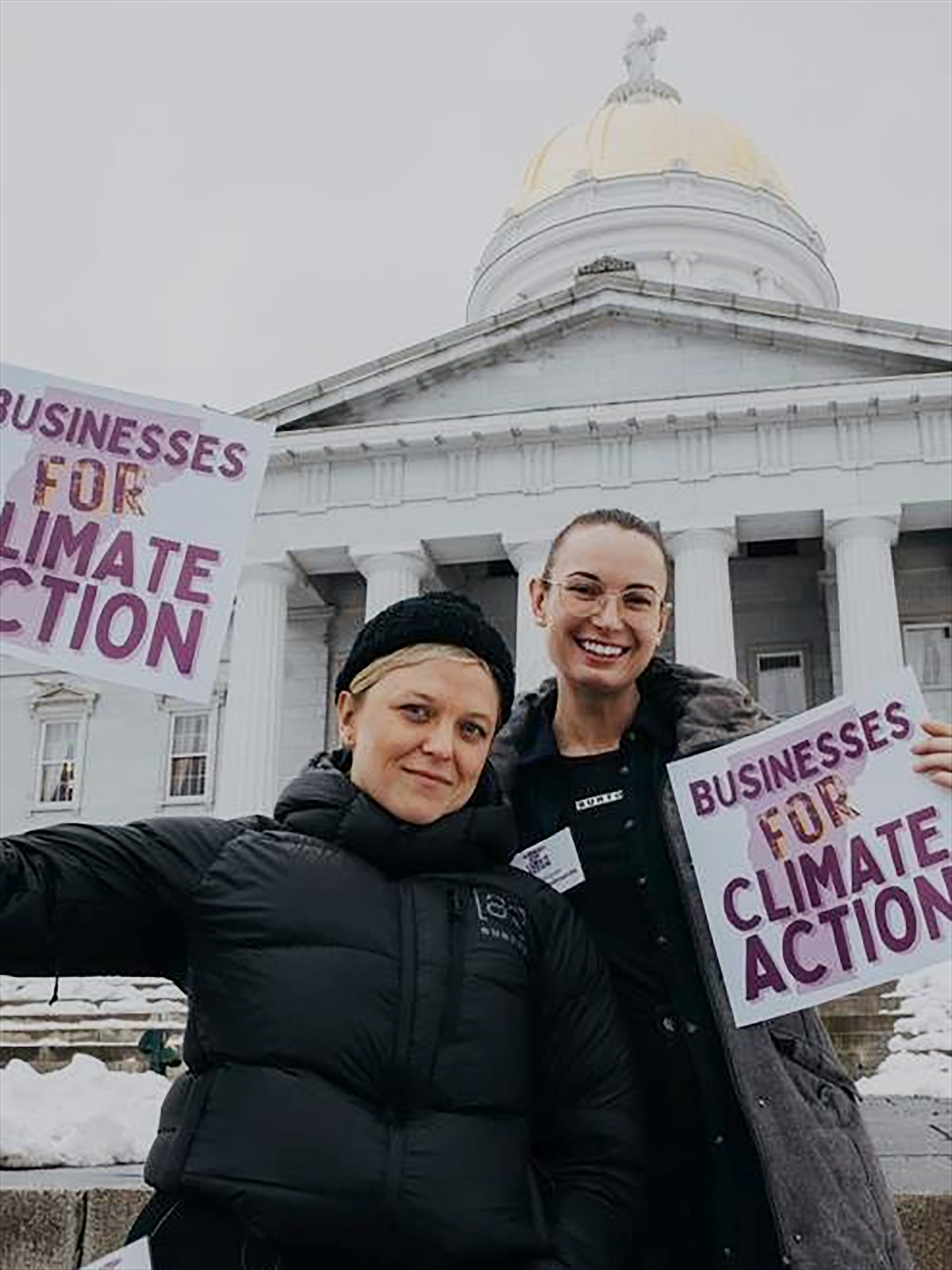 Two people holding signs advocating for climate action in front of a government building.