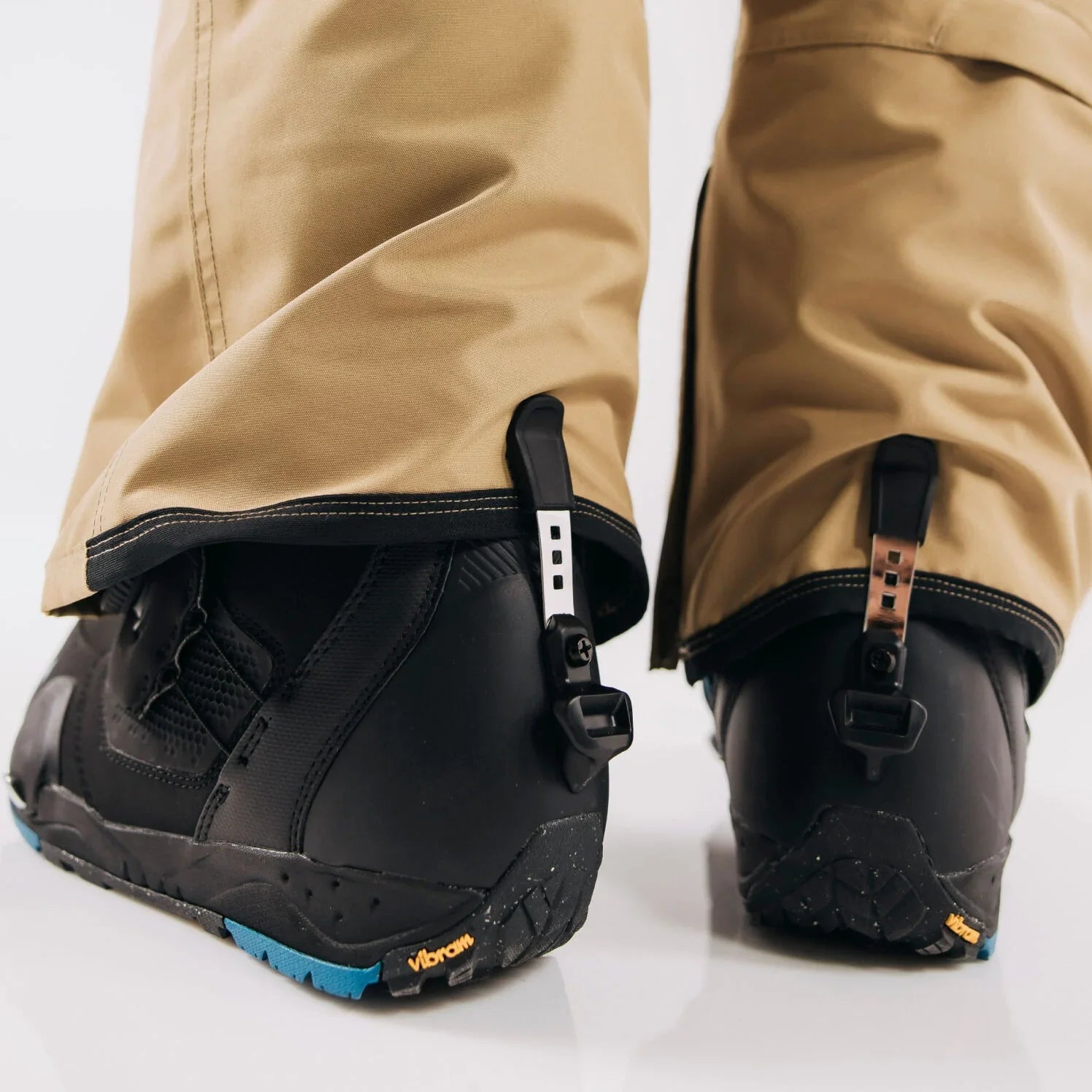 Close-up of cuff clips on black boots with beige pants on a white background