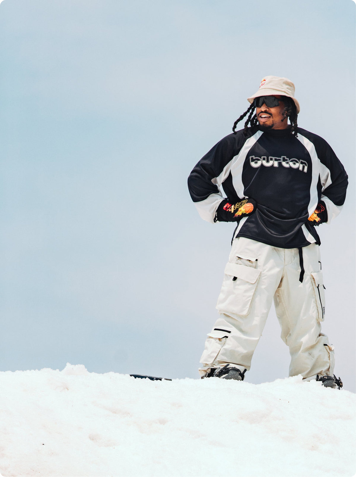 rider zeb pictured hands on hips with mittens on wearing a black and white burton jersey on snow