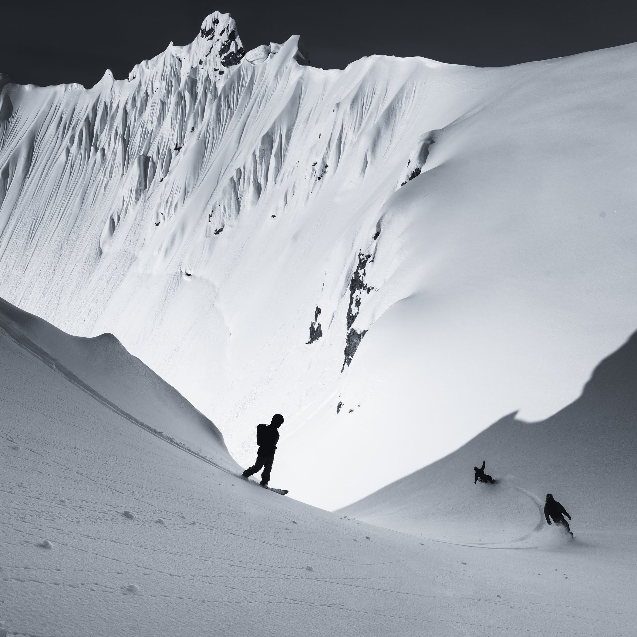 Snowboarders taking turns down a steep slope