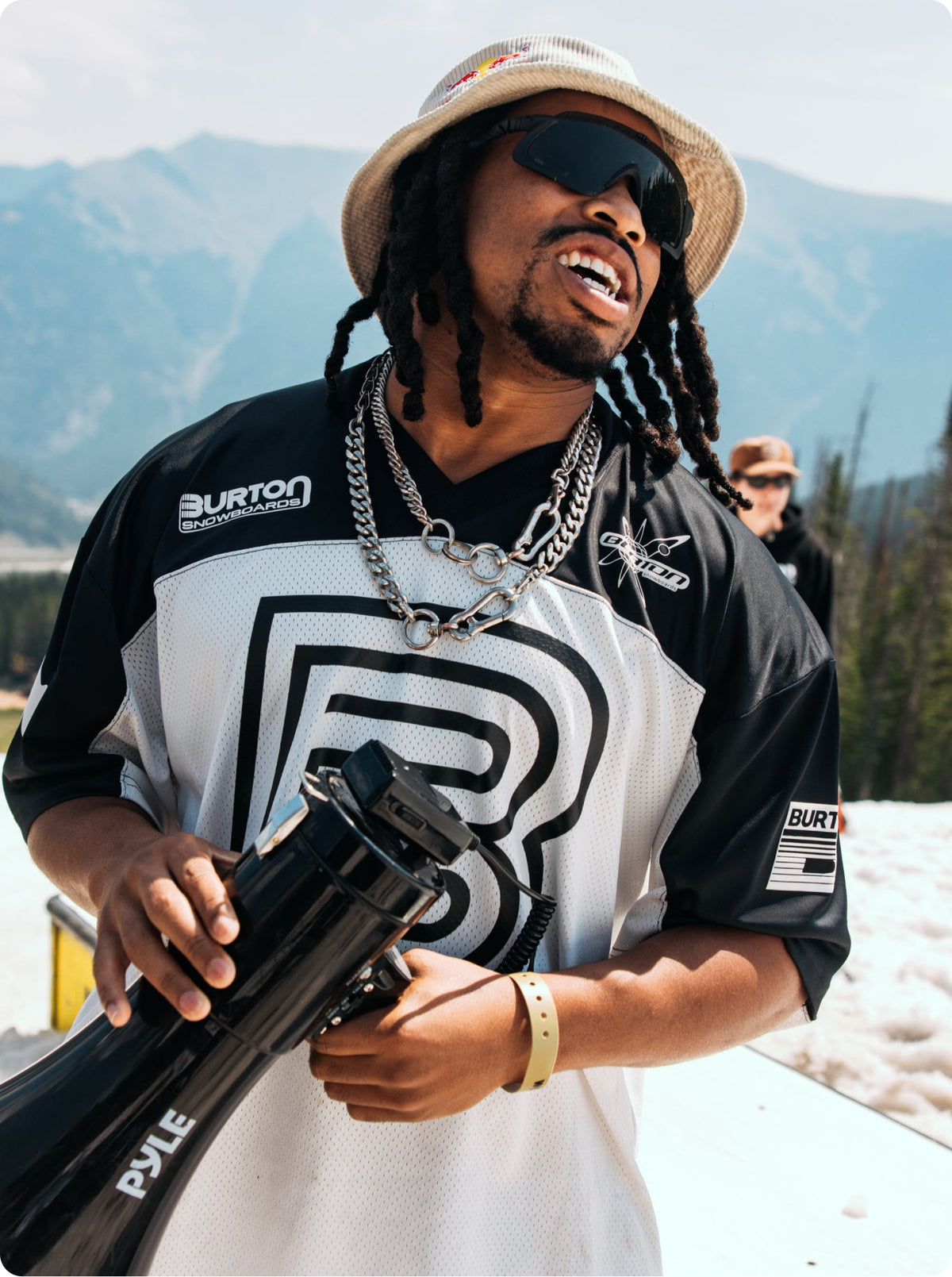 zeb with megaphone in front of mountains. wearing a burton team jersey.